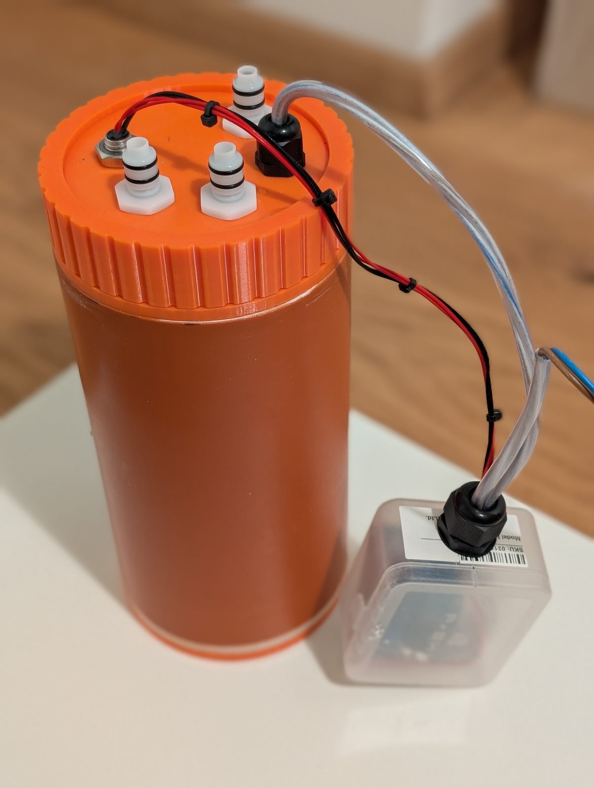 Six years, in one photograph. A €7 length of drainpipe, four printed parts, and a small clear box that does the thinking. The finished sump standing on a table before installation, controller box beside it