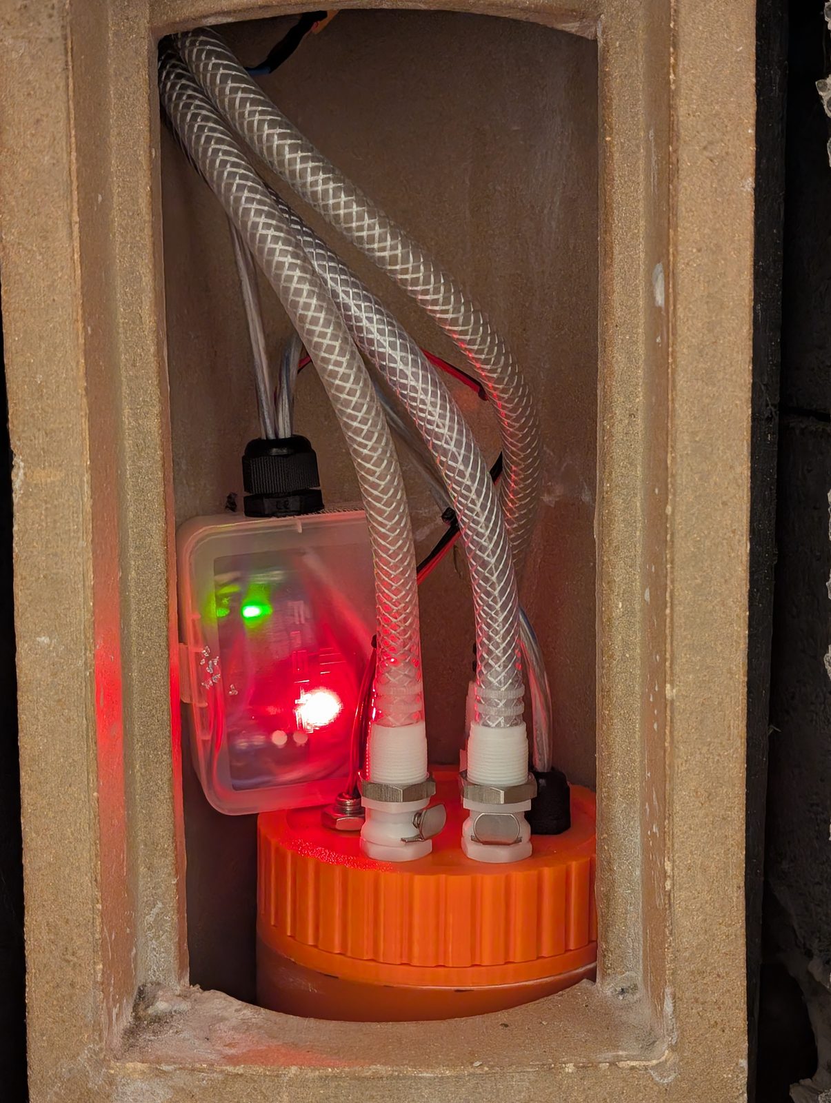 In position, viewed through the chimney door. The red glow is the controller, minding its own business. The sump installed at the bottom of the chimney, hoses connected, controller glowing beside it